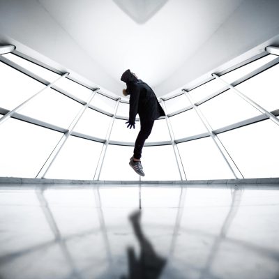 A person seemingly levitates in a contemporary room with reflections and shadows.