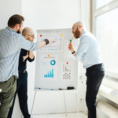 Three business professionals discussing financial charts and reports indoors during the day.